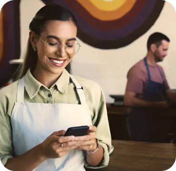 Mesera sonriente en una cafetería usando celular para cobrar con Poket